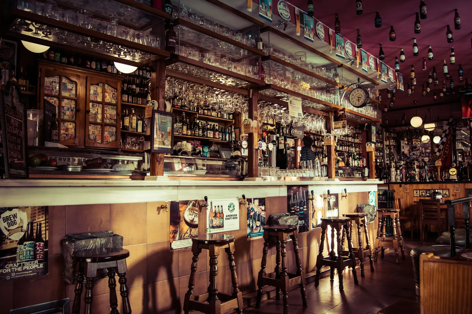 La barra por dentro: taburetes de madera, copas colgadas y las botellas al fondo