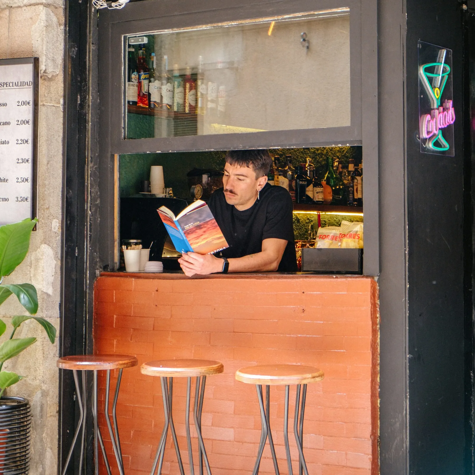 La ventana que da a la calle, con un camarero leyendo mientras espera y tres taburetes delante