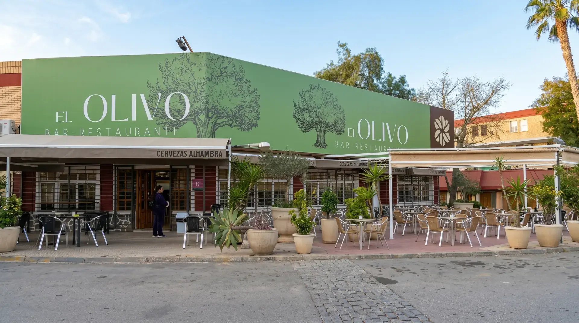 La fachada verde de El Olivo con su rótulo y la terraza con mesas y macetas, en la avenida Primero de Mayo