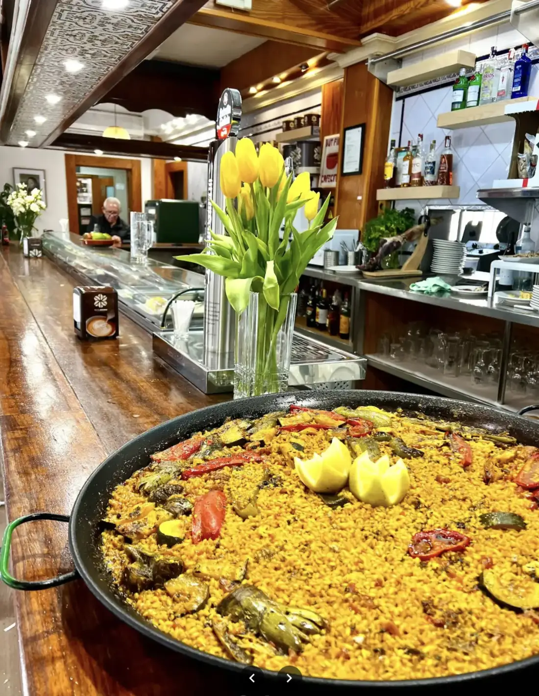Una paella con limón recién puesta sobre la barra de madera, junto a un jarrón de tulipanes amarillos
