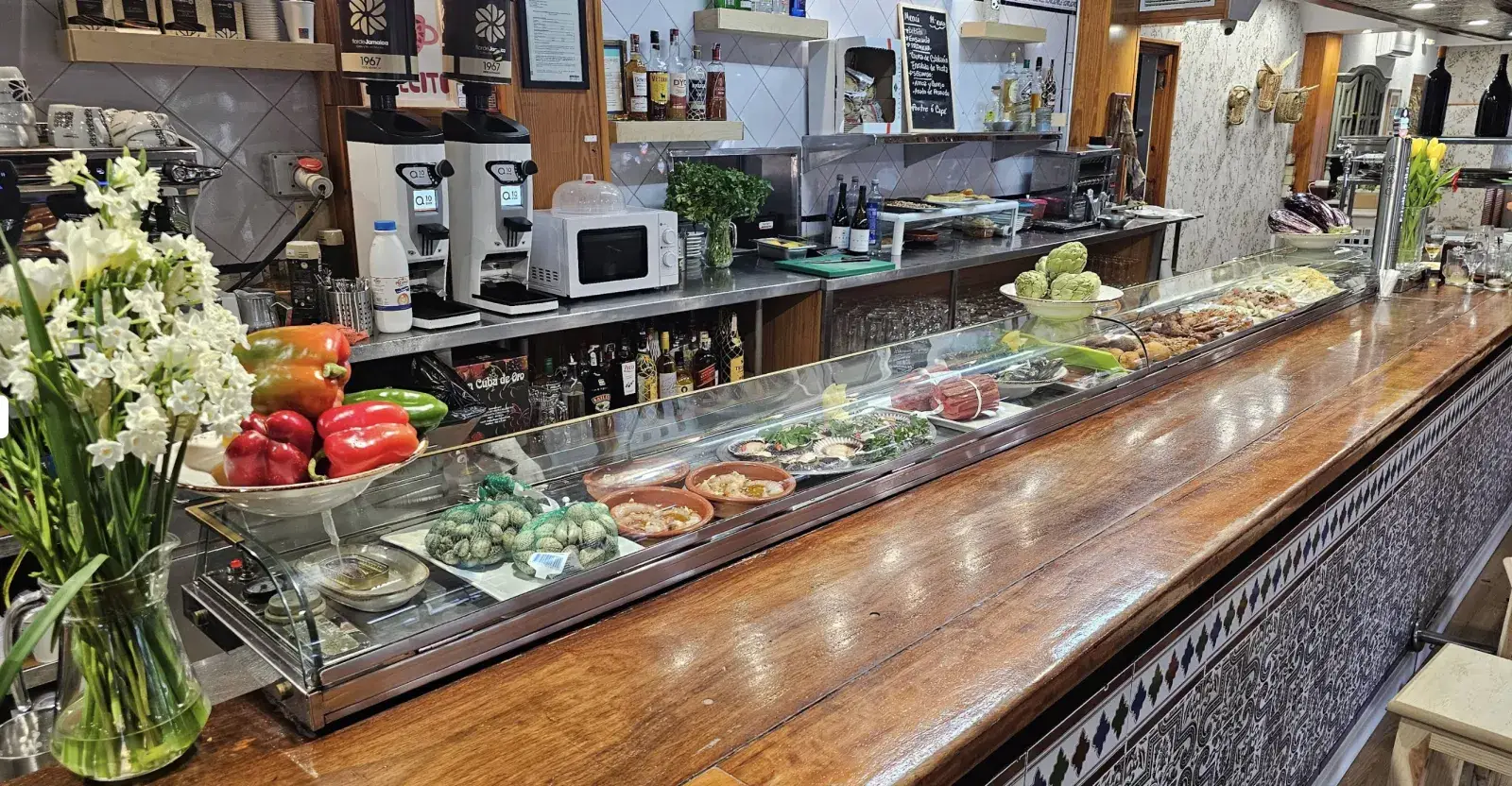 La vitrina de tapas a lo largo de la barra, con flores blancas en primer plano